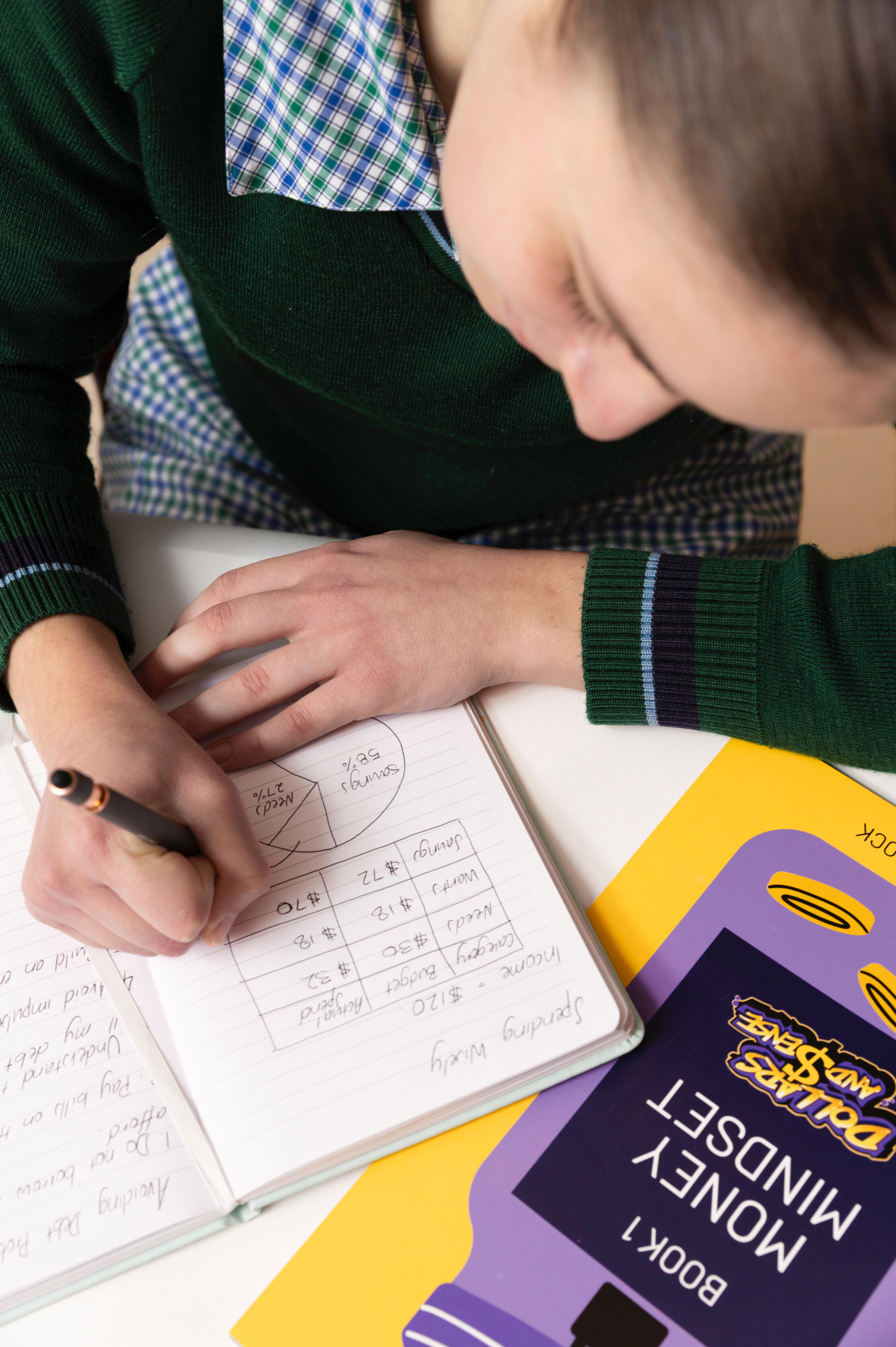 Financial Literacy 101 photo A school student is writing down financial plans with an open book.